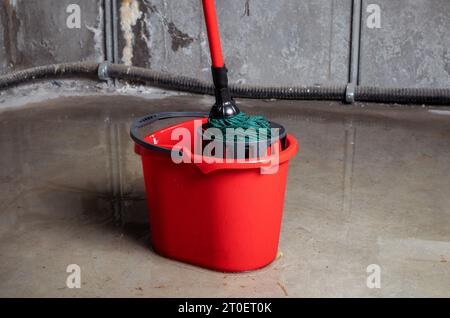 Eimer mit Mob im überfluteten Keller oder Elektroraum. Reinigen Sie viel Wasser auf dem Boden von mehreren Lecks in Wand und Decke. Wasserschäden durch Stockfoto