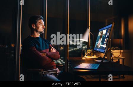 Der Unternehmer arbeitet spät in seinem Heimbüro und nimmt an einer Videokonferenz mit seinen Kollegen Teil. Geschäftsmann diskutiert Arbeitsprojekte in einem virtuellen Meeting Stockfoto