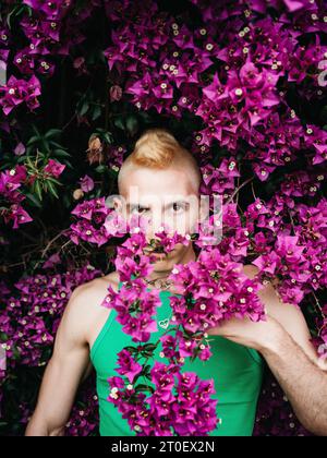 Nicht-binäre Person mit grüner Spitze steht vor einem Sträucher mit Blumen Stockfoto