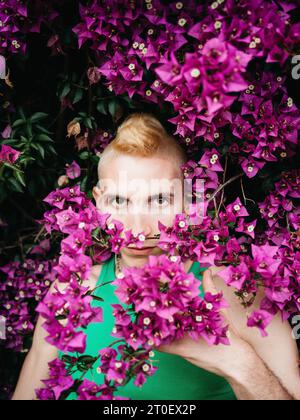 Nicht-binäre Person mit grüner Spitze steht vor einem Sträucher mit Blumen Stockfoto