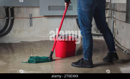 Frau wischt Flutwasser von Wasserlecks im Keller oder Elektroraum ab. Wasserschäden durch Regen, Schneeschmelze oder Rohrplatzen durch mehrere Risse und Risse Stockfoto