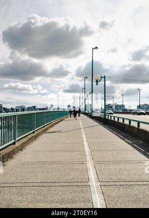 Rückansicht der Fußgängerbrücke mit Stadthintergrund an einem sonnigen Frühlingstag. Lange Brücke mit gemeinsamem Bürgersteig und Fahrspuren. Cambie Stockfoto