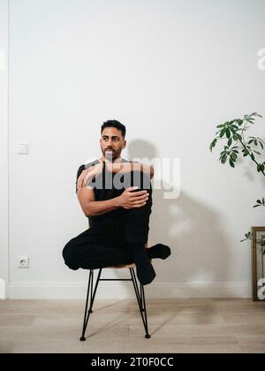 Nicht binäre Person mit schwarzem T-Shirt auf dem Stuhl Stockfoto