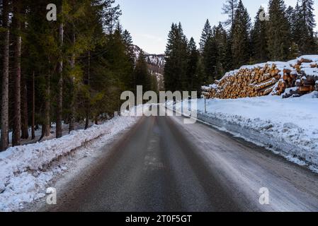 Gerade Strecke einer eisigen Bergstraße, die im Winter bei Dämmerung durch einen verschneiten Wald führt Stockfoto