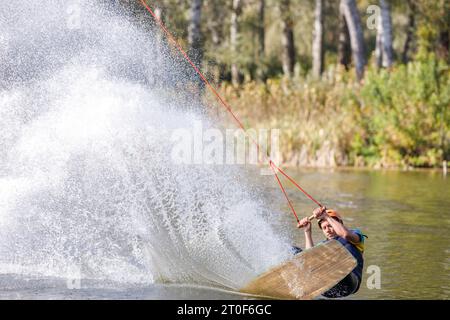 Sportler auf dem Wakeboard, der nach einem Trick auf den Rücken fällt und viele Spritzer aufwirft Stockfoto