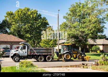 Ein Mitarbeiter der Wasserabteilung von Wichita Kansas gräbt eine Wasserleitung mit John Deere Baggerlader mit Bulldozer in einem Stadtviertel aus. Wichita, Kansas, USA. Stockfoto