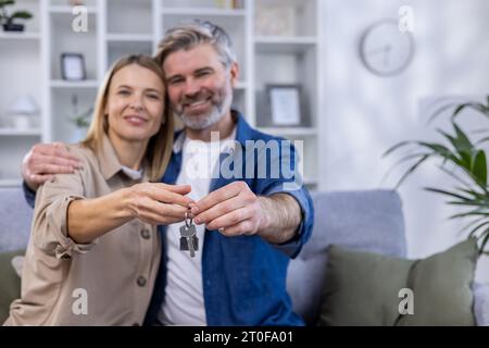 Ausgewählter Fokus, älteres grauhaariges Paar, Mann und Frau, die sich in einem neuen Wohnhaus umarmen, glückliche Familie, die Hausschlüssel hält. Stockfoto