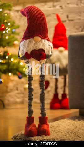 Weihnachtsbaum mit Weihnachtsmann-Spielzeug. Weihnachtself mit Herz auf festlichem Hintergrund. Neujahrsgrüße. Skandinavischer Elf mit rotem Hut. Winterurlaub Stockfoto