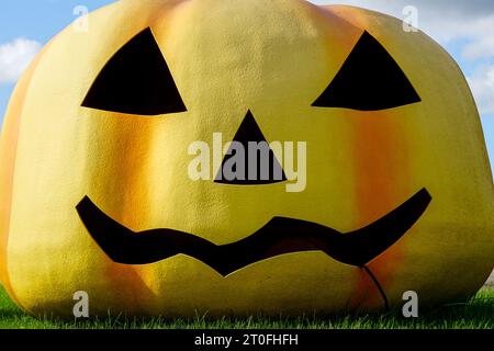 Ein riesiger Fiberglas-Kürbiskopf im Halloween-Stil mit einem lächelnden Gesicht unter freiem Himmel, Halloween-Kürbiskopf aus Fiberglas im Freien Stockfoto