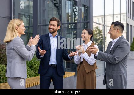 Geschäftsleute außerhalb des Bürogebäudes applaudieren und gratulieren dem Vorgesetzten mit Beförderung und guten Ergebnissen, vier Personen, Frauen und Männer, die im Freien eine Pause machen. Stockfoto