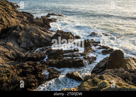 Wellen brechen auf Felsen in der Nähe von Rhosneigr an der Westküste von Anglesey, Nordwales. Stockfoto