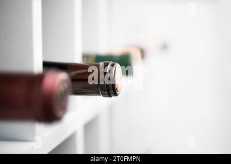 Auswahl an Weinflaschen in Weinregal mit weißem Hintergrund. Selektiver Fokus auf eine Flasche mit defokussierten Flaschen. Verschiedene Weine in elegantem Holz Stockfoto