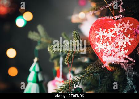 Herzschmuck auf dem Weihnachtsbaum mit defokussiertem Hintergrund und Bokeh-Lichtern. Frohe Weihnachten Hintergrundkonzept. Große rote Herzdekoration mit funkelndem Glitzer Stockfoto