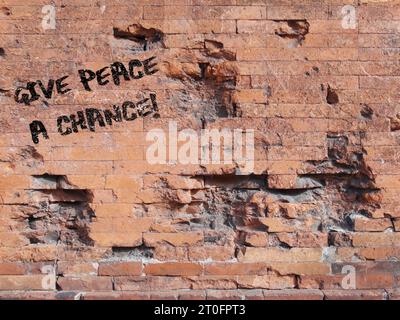 Phrase Give Peace a Chance Spray in weiß auf eine beschädigte Ziegelwand gemalt Stockfoto