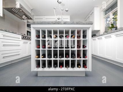 Auswahl an Weinflaschen im Weinregal der Kücheninsel. Weinauswahl in elegantem Holzregal in moderner weißer Küche. Moderner Weinhintergrund Stockfoto