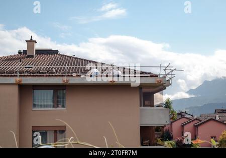 Auftragnehmer arbeiten auf dem Dach mit Keramikfliesen in einem 4-stöckigen Wohngebäude. Die Arbeiter haben ein Sicherheitsgeländer, aber kein Seil. Dachreparaturarbeiten Selektiv f Stockfoto