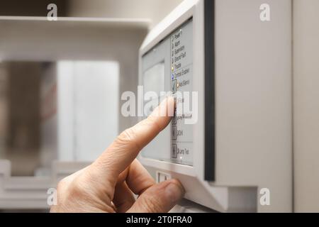 Feuermeldetechniker, der die Brandmeldezentrale oder den Melder verwendet. Der Finger befindet sich auf der Reset-Taste auf dem Bedienfeld im Serviceraum oder in der Lobby von Re Stockfoto