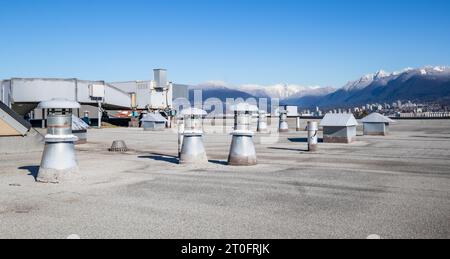 Flache Dachentlüftungen mit hlk-Anlage im Gebäude mit modifiziertem Bitumendachsystem mit schneebedeckten Bergen. Auswahl an Metallventilatoren, z. B.: Bade Stockfoto