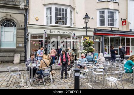 Wells, Großbritannien, 4. August 2023: Geschäftige Hauptstraße mit Menschen, Cafés und anderen Geschäften und Eingang zum Bischofspalast. Stockfoto