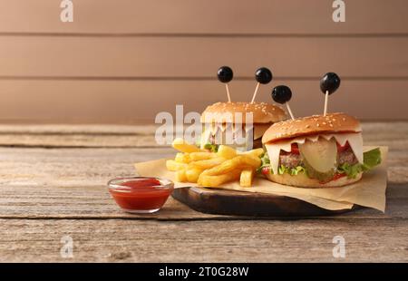 Niedliche Monster Burger serviert mit Pommes frites und Ketchup auf Holztisch, Platz für Text. Halloween Party Essen Stockfoto