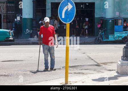 Ein ranghoher kubanischer Mann überquert die unebene Straße oder Allee mit einem Gehstock. Stockfoto