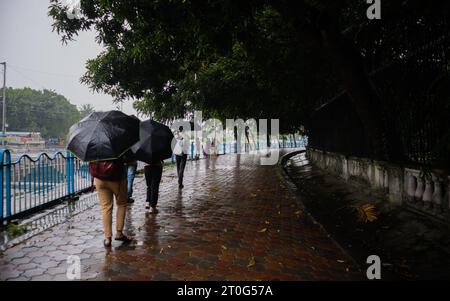 Menschen, die mit einem Regenschirm auf einem regennassen Fußweg und während der Monsunsaison in den Straßen von kalkutta indien spazieren. Stockfoto