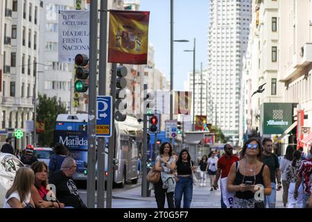 Madrid, Spanien. Oktober 2023. Touristen und Fußgänger spazieren auf dem Bürgersteig der Calle Gran, wo die Straße vor dem spanischen Nationalfeiertag in Madrid mit einer spanischen Flagge geschmückt ist. Der Madrider Stadtrat installierte Banner und die spanische Flagge zur Feier des spanischen Nationalfeiertags, der jeden 12. Oktober gefeiert wird. Der Tag ist auch bekannt als Dia dela Hispanidad. Quelle: SOPA Images Limited/Alamy Live News Stockfoto