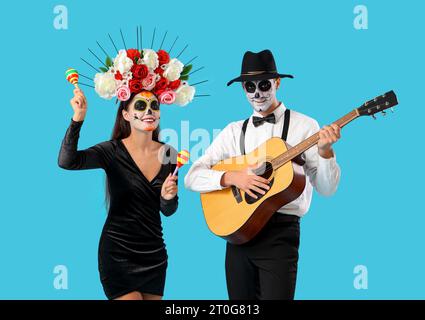 Junges Paar gekleidet für Mexikos Tag der Toten (El Dia de Muertos) mit Gitarre auf blauem Hintergrund Stockfoto