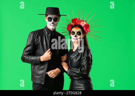 Junges Paar, das für Mexikos Tag der Toten (El Dia de Muertos) auf grünem Hintergrund gekleidet ist Stockfoto