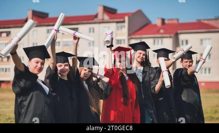 Junge Absolventen posieren und winken Diplome in den Händen auf der Straße. Stockfoto