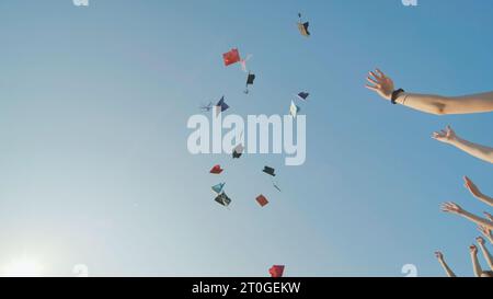 Absolventen werfen bunte Hüte gegen einen blauen Himmel. Stockfoto