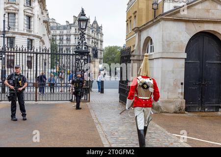 Der Pferdewächter in zeremonieller Kleidung geht in Richtung der Nähe bewaffneter Metropolitanpolizisten im Horse Guards Building Whitehall, London, England Stockfoto
