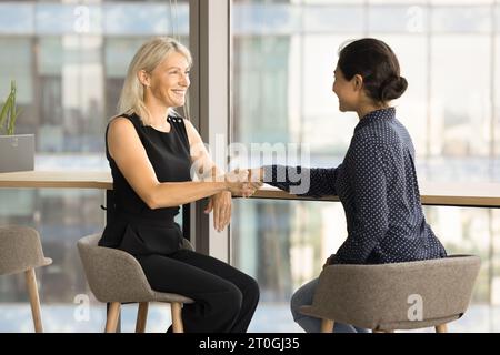 Fröhlich zufriedene jüngere und ältere Kollegen Frauen, die Hand schütteln Stockfoto