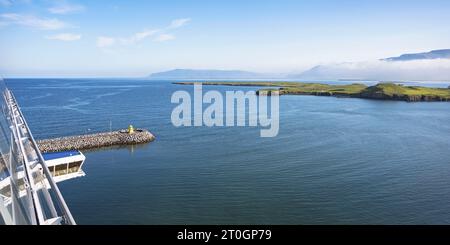 Der Leuchtturm Skarfagardur befindet sich unter dem Geländer eines Kreuzfahrtschiffes mit Videy Island und einem wunderschönen Himmel im Hintergrund und Wasser im Vordergrund Stockfoto