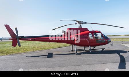 Kleiner roter Touristenhubschrauber auf dem Boden eines Flughafens mit einem klaren blauen Himmel im Hintergrund und Asphalt im Vordergrund Stockfoto