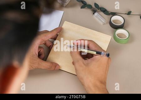 Junge Hände halten und schreiben auf Holzkartonkarte beigefarbenen Hintergrund. Foto und leeres Produkt auf Lager Stockfoto