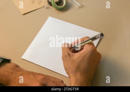 Junge Hände halten und schreiben auf Holzkartonkarte beigefarbenen Hintergrund. Foto und leeres Produkt auf Lager Stockfoto