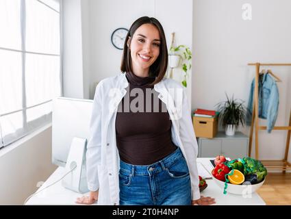 Lächelndes Porträt einer jungen Ernährungsärztin, die am Schreibtisch steht Stockfoto