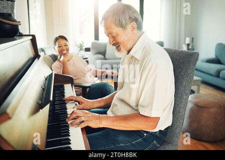 Senior-Mann spielt Klavier für Musik im Wohnzimmer mit seiner Frau, um sich zu unterhalten, zu unterhalten oder Spaß zu haben. Glücklich, lächelnd und älteres asiatisches Paar Stockfoto