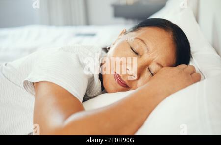 Reif, Frau und ruhig im Bett mit gutem Traum, Kopfkissen und Frieden. Asiatisch, ältere Person und Gesicht im Schlafzimmer, allein und lächelnd Stockfoto