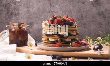 Pfannkuchen mit Banane, Heidelbeeren, Erdbeeren und Schokoladensauce auf einem Teller. Stockfoto