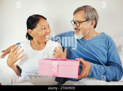 Senior, Mann und Frau mit Geschenk im Schlafzimmer zum Jubiläum, romantisch oder zusammen. Asiatisches, älteres Paar und Band durch Lächeln in Glück zum Feiern Stockfoto