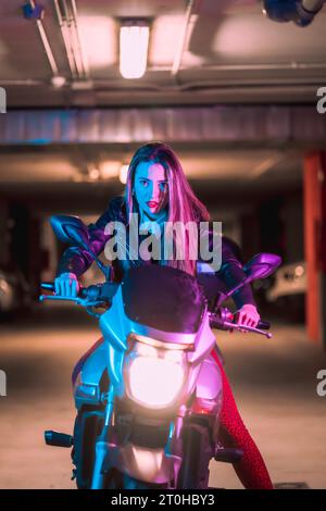 Fotografie mit blauen und rosa Neonfarben auf einem Motorrad. Porträt eines jungen blonden kaukasischen Models mit schwarzer Lederjacke Stockfoto