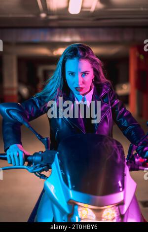 Fotografie mit blauen und rosa Neonfarben auf einem Motorrad. Porträt eines jungen blonden kaukasischen Models mit schwarzer Lederjacke Stockfoto