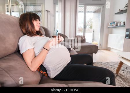 Junge schwangere Frau mit Schwangerschaftsdiabetes Selbsttest, um den Zucker auf dem Sofa zu Hause zu kontrollieren und den Bluttropfen aus ihrem Finger zu messen Stockfoto