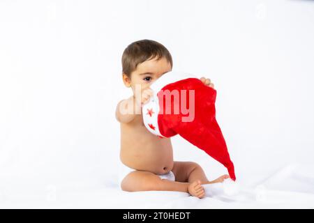 Ein kleiner Junge mit einem roten Weihnachtshut auf weißem Hintergrund, Platz kopieren und mit dem Hut des Weihnachtsmanns spielen Stockfoto