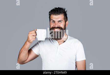 Gutaussehende Männer halten eine Tasse Kaffee und Tee. Bärtiger Mann lächelt. Guten Morgen, Mann Tee. Lächelnder Hipster-Mann mit einer Tasse frischen Kaffee, glücklicher Mann. Vormittag Stockfoto