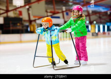 Skateboard für Kinder auf einer Eislaufbahn. Skaten für Kinder. Aktiver Familiensport im Winterurlaub und in der kalten Jahreszeit. Kleines Mädchen und Junge in farbenfroher Kleidung Stockfoto