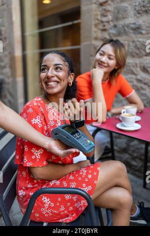 Glückliche Frau, die auf einer Terrasse mit intelligenter Uhr bezahlt Stockfoto