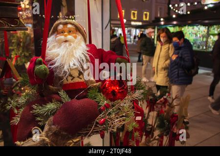 Weihnachtsmann-Puppe auf dem Weihnachtsmarkt. Weihnachtsmann mit Geschenken und unbekannte Menschen in Masken. Quarantäne-Weihnachtsmarkt. Weihnachtseinkäufe in Europa. Stockfoto